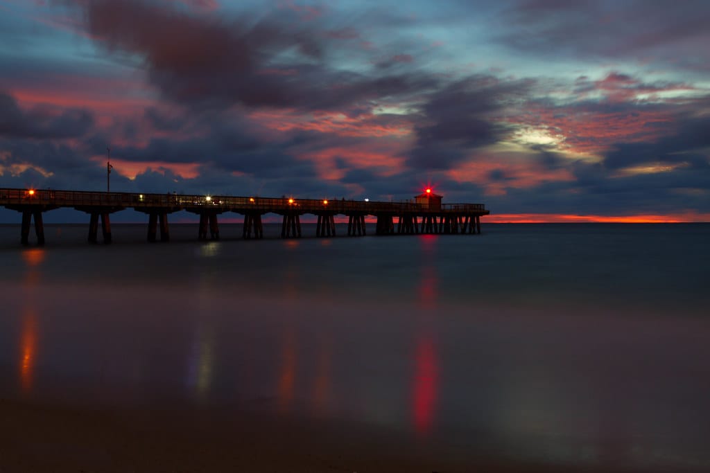 The Pompano Beach fishing pier stretching into the Atlantic beneath a pink and violet sky before sunrise