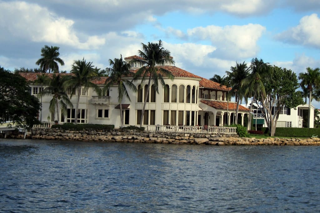 A Mediterranean-style waterfront home with a seawall and palms beside open water in Fort Lauderdale